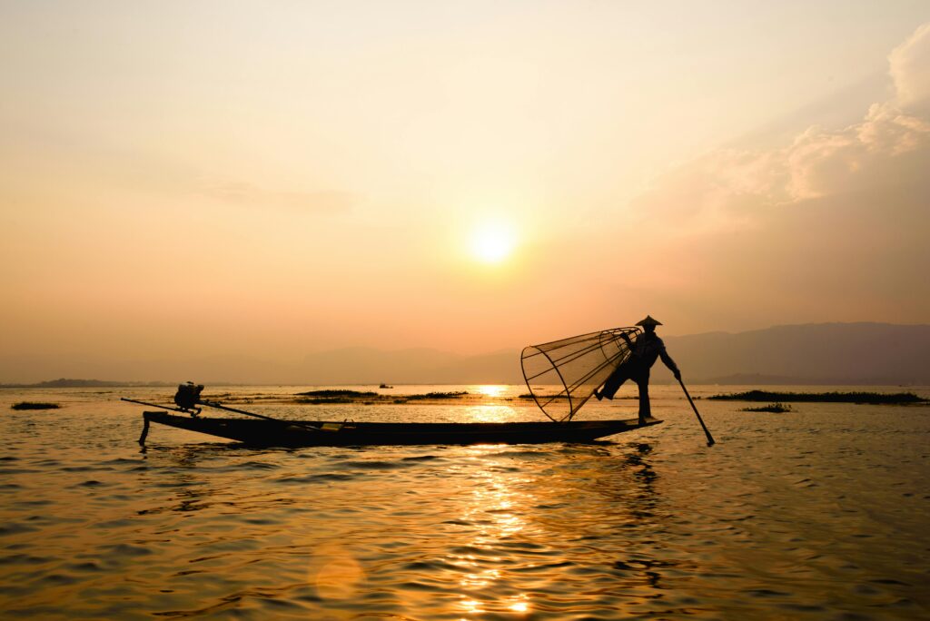 Silhouette of a fisherman balancing on a boat with the sun rising over Inle Lake, Myanmar.